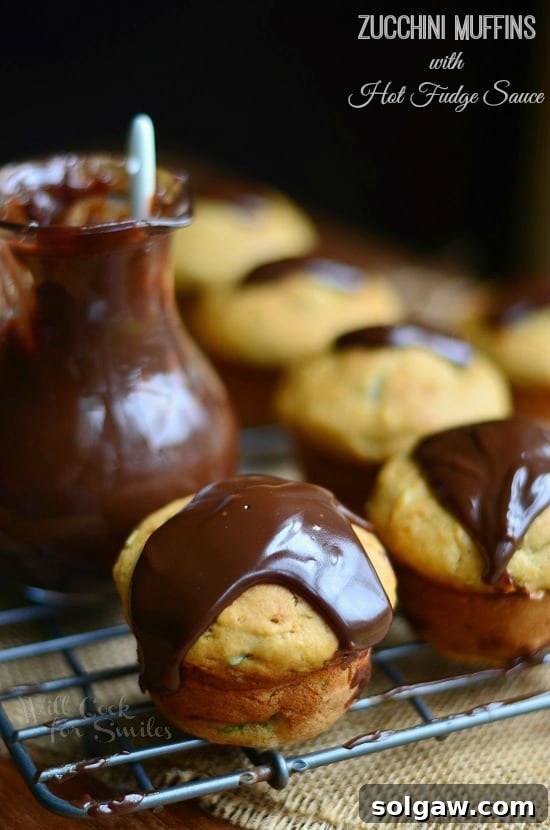 A close-up of a Zucchini Muffin topped with Hot Fudge Sauce, showing its moist texture, on a cooling rack.