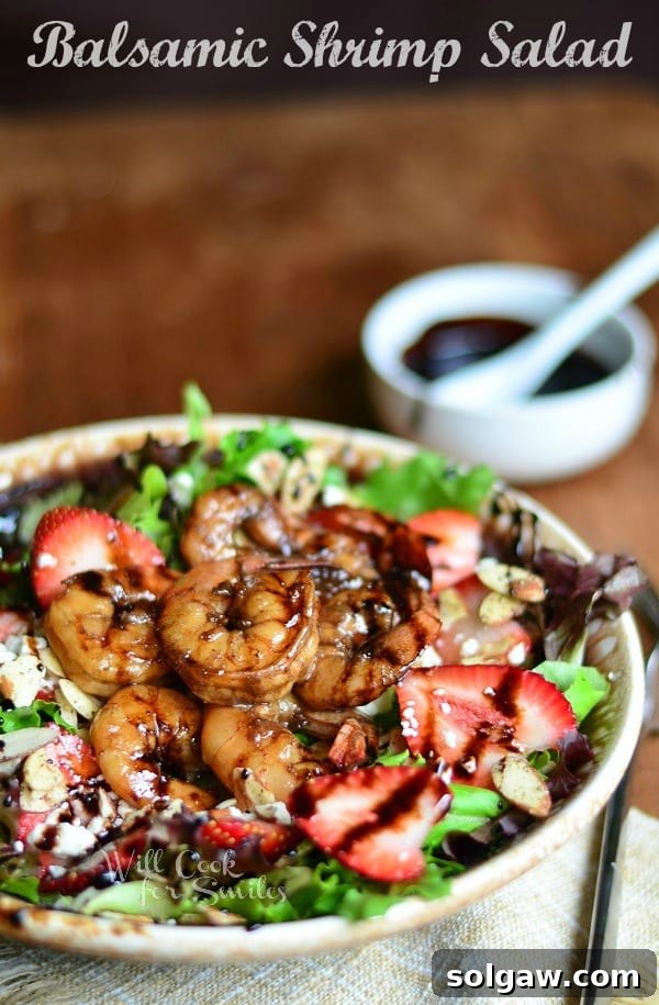 Balsamic Shrimp Salad on a brown plate with shrimp and strawberries and a bowl of dressing at the top right