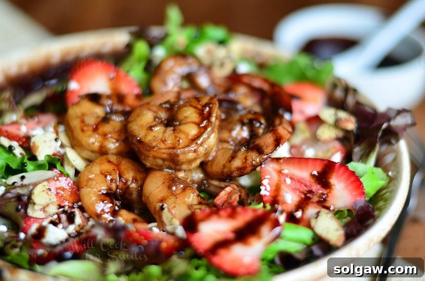 Horizonal photo Balsamic Shrimp Salad on a brown plate with shrimp and strawberries and a bowl of dressing at the top right