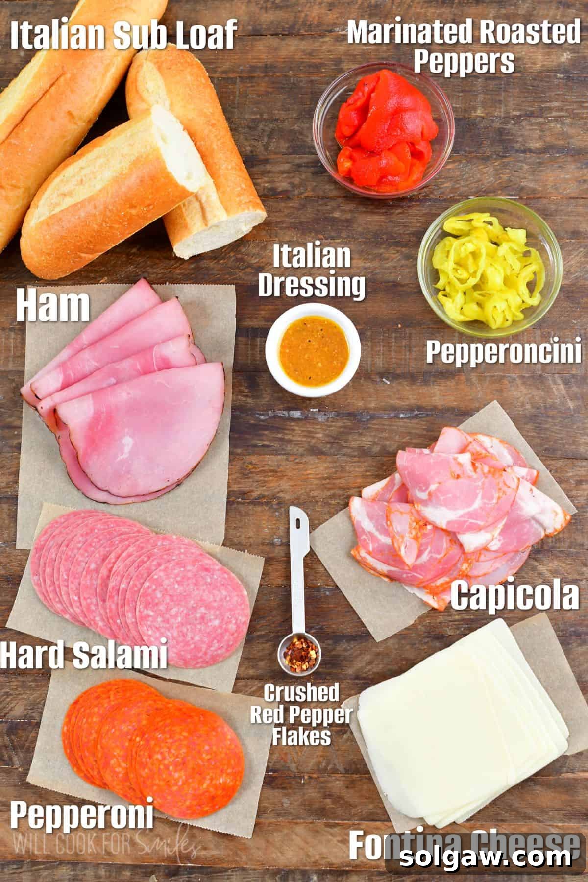 An assortment of fresh Italian sub ingredients, including various deli meats, cheese, peppers, and a rustic loaf of bread, laid out on a wooden surface.