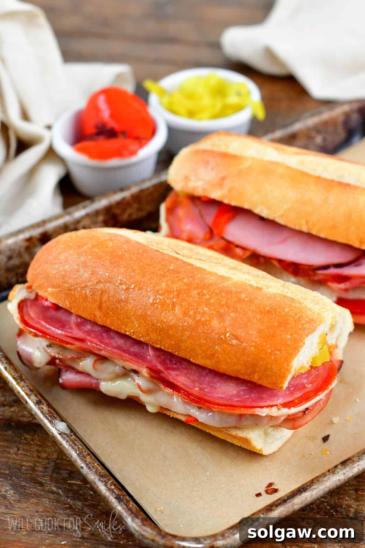 Two freshly baked Italian subs resting on parchment paper on a baking sheet, golden brown and enticing.