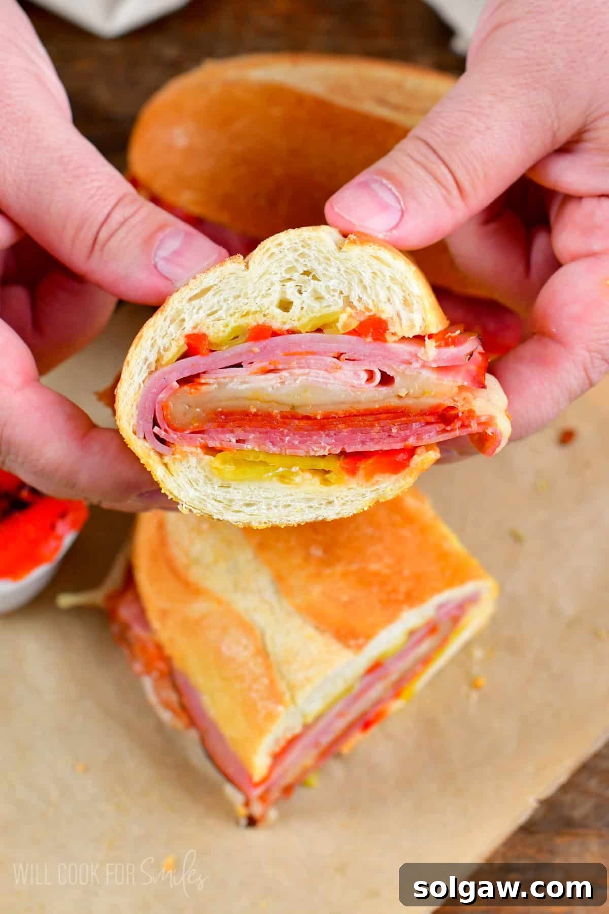 A hand gracefully holding half of a freshly baked Italian sub, beautifully showcasing its rich, layered fillings.