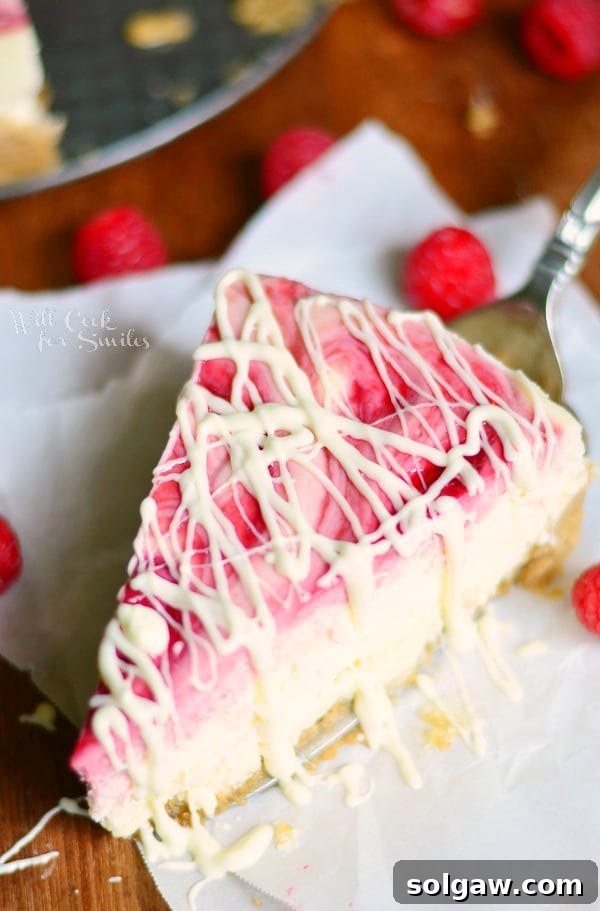 Decadent White Chocolate Raspberry Swirl Cheesecake 5 above view of 1 slice of white chocolate raspberry swirl cheesecake with berries around slice and whole cake in oan above to the left