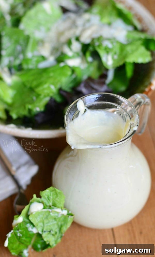 Homemade Light Caesar Dressing in a glass cruet next to a fresh Caesar salad bowl, ready to be served.