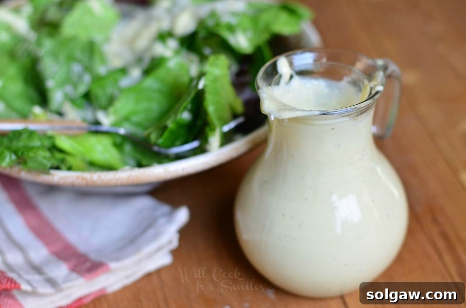 Top-down view of a light Caesar dressing in a glass bottle with a fresh Caesar salad featuring crisp romaine, homemade croutons, and Parmesan shavings.