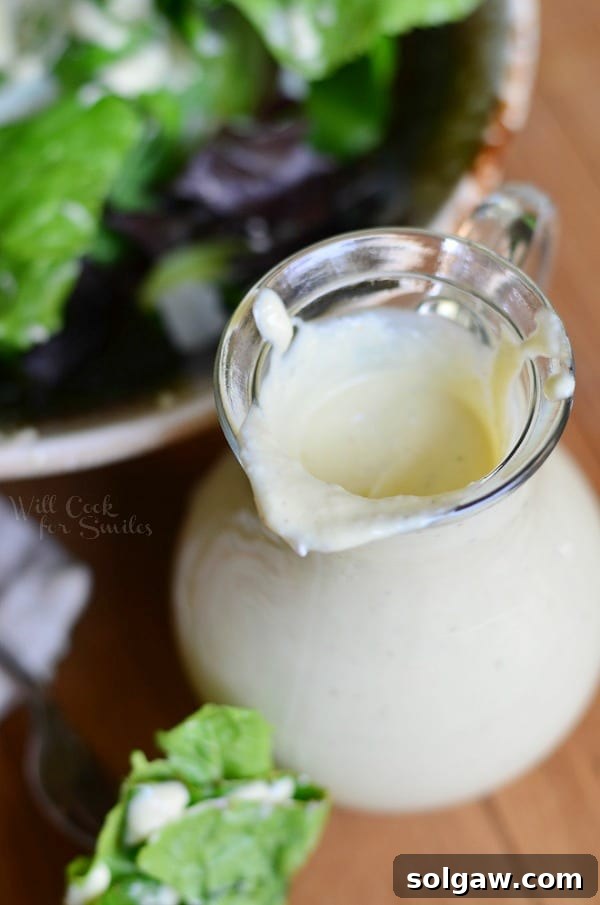 Overhead shot of a glass cruet filled with light Caesar dressing, accompanied by a bowl of fresh Caesar salad with romaine lettuce and croutons.
