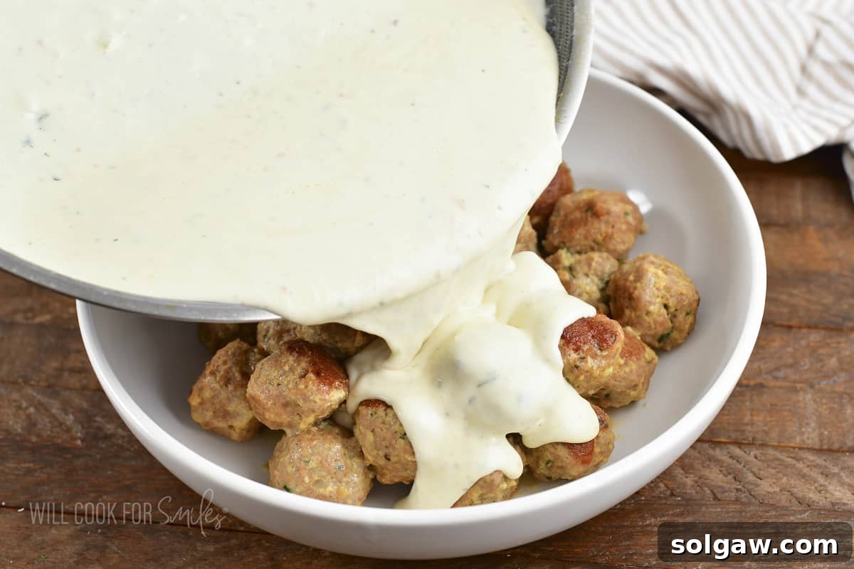 pouring parmesan cream sauce over the meatballs.