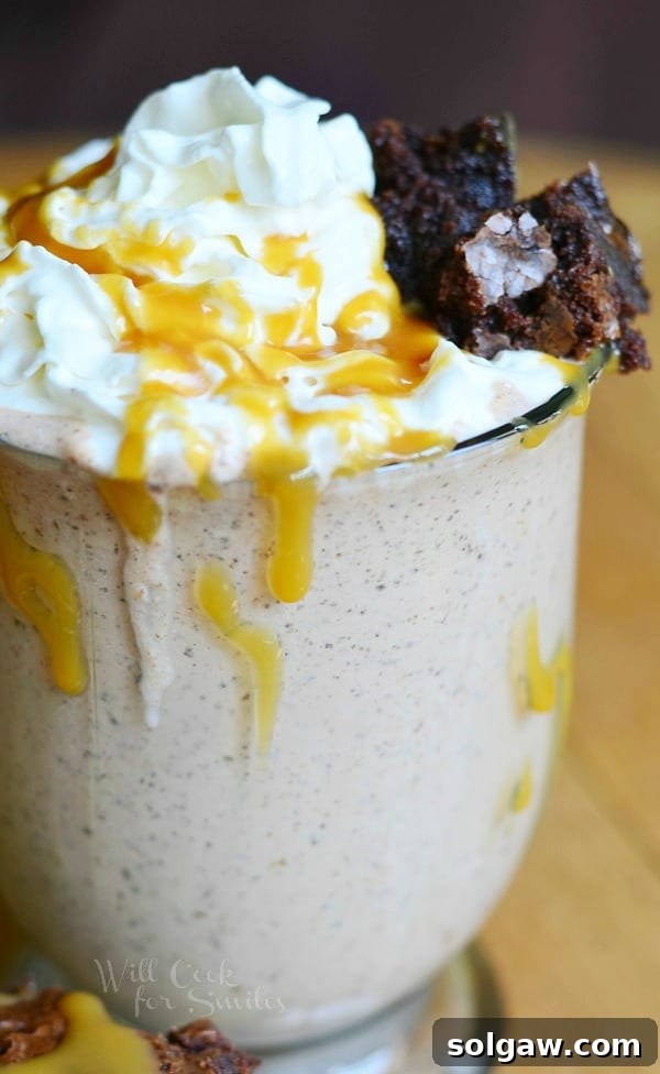 Salted Caramel Brownie Milkshake presented beautifully in a glass, crowned with fluffy whipped cream, adorned with a luxurious caramel topping, and a piece of brownie on top.