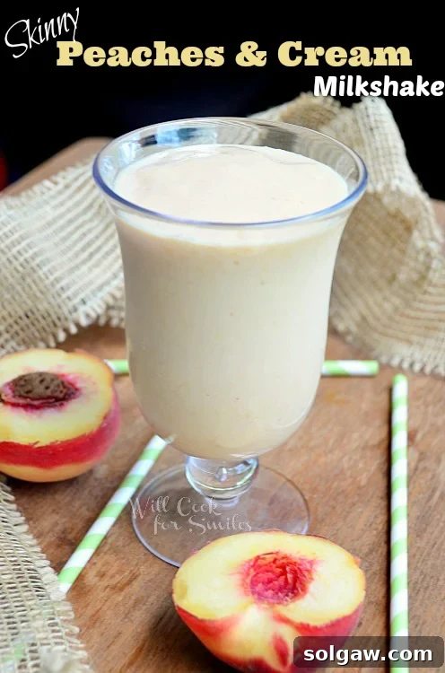 Peaches and Cream Milkshake in a glass, surrounded by sliced peaches and green and white straws on a table.