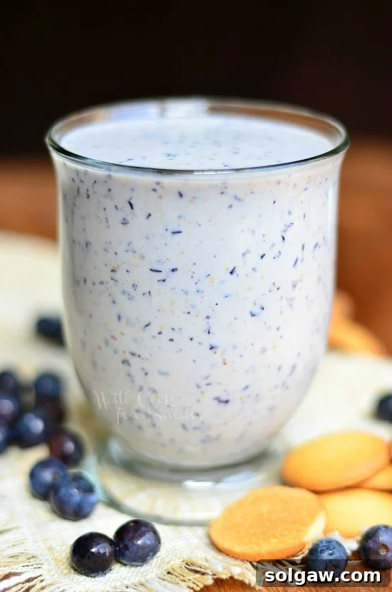 Blueberry Muffin Milkshake in a glass, with fresh blueberries and vanilla wafers scattered around on the table.