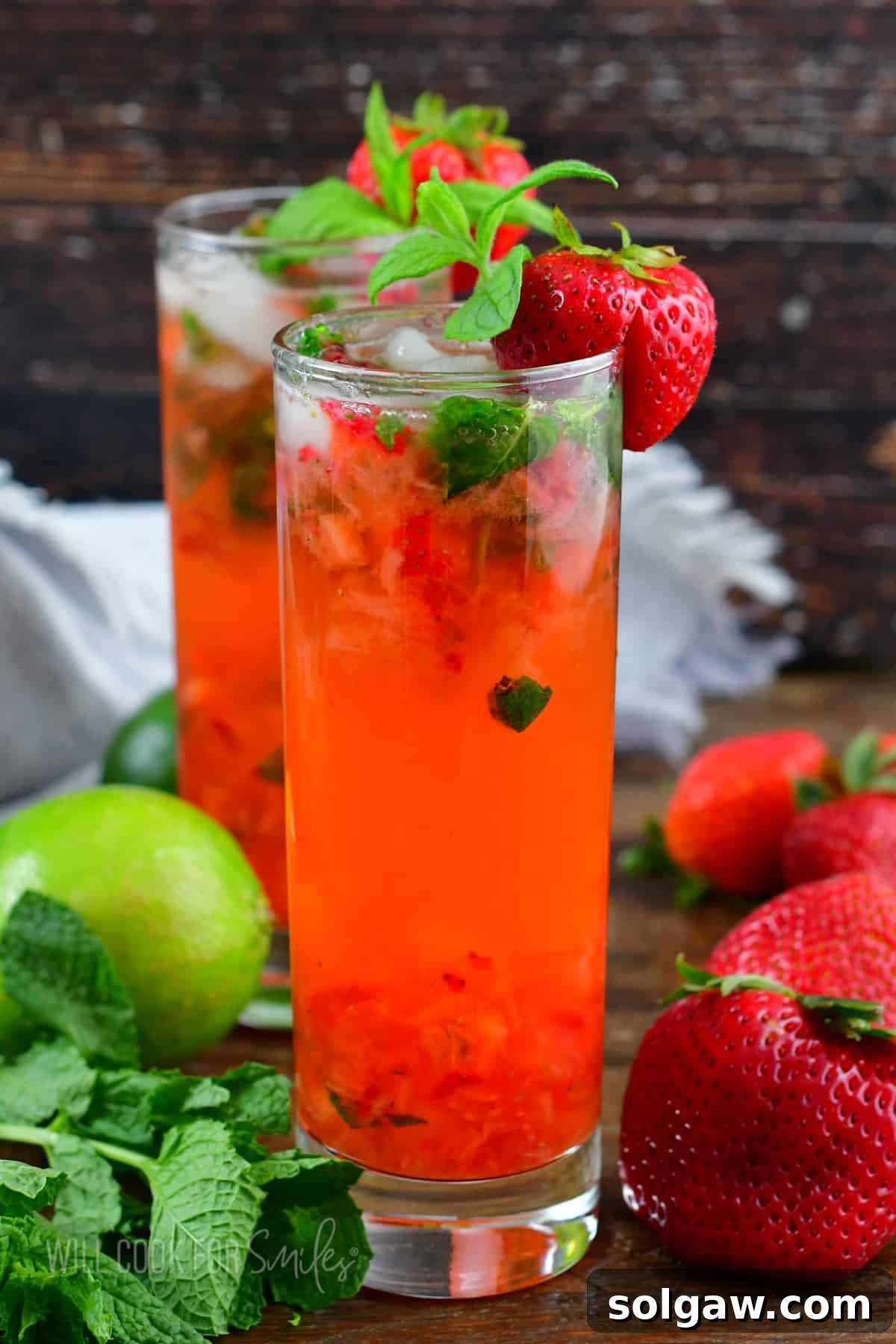 tall glass with bright pink strawberry cocktail with mint and strawberries around.