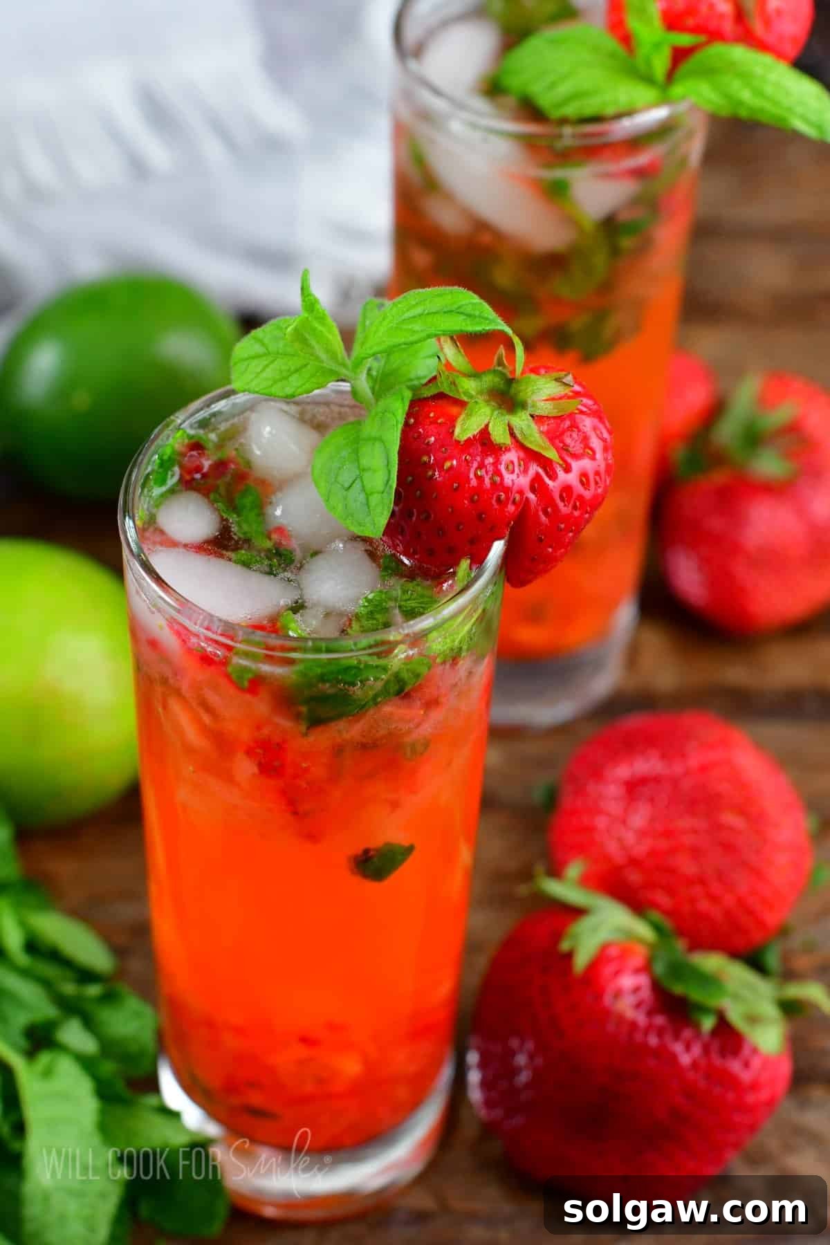 two glasses with bright strawberry mojito cocktails and berries around on the table.