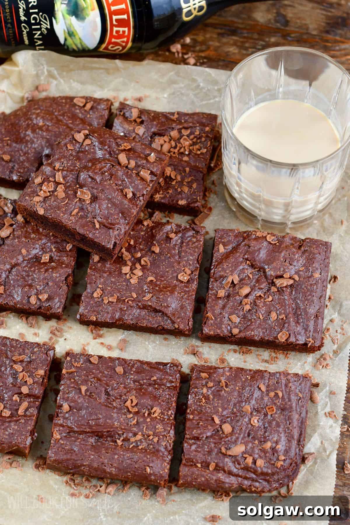 Bailys brownies cut into squares on a piece of parchment paper with a glass with baileys in it.
