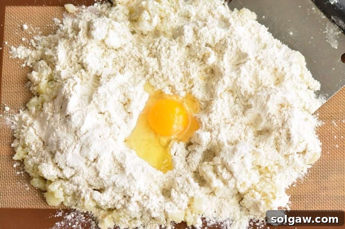 Pillowy Homemade Gnocchi Perfection 4 A mount of smashed cooked potatoes with flour and an egg in the center on a wooden board, ready to be mixed for gnocchi dough.