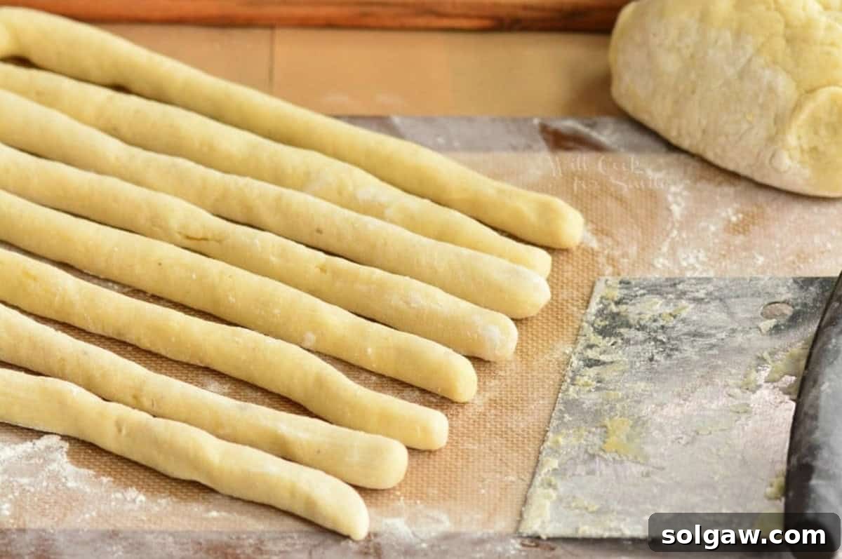 Pillowy Homemade Gnocchi Perfection 6 Rolled strips of gnocchi dough on a floured mat next to more dough and a pastry cutter, ready for cutting.