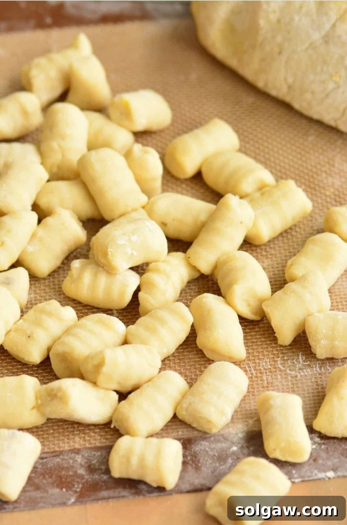 Pillowy Homemade Gnocchi Perfection 10 Rolled pieces of gnocchi on a silicone mat next to another half of dough, showcasing the preparation process.