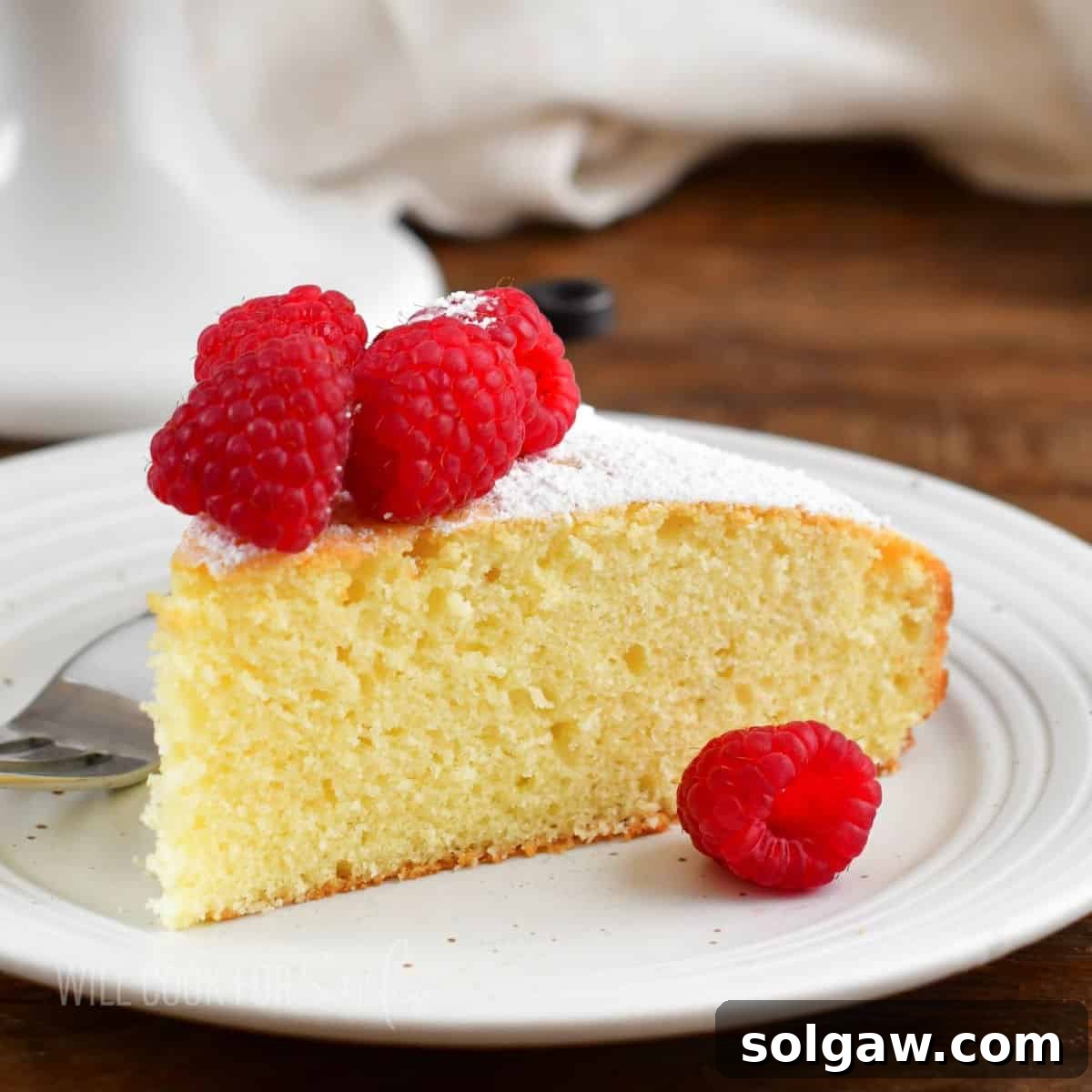 Closeup of a moist and fluffy Irish tea cake on a white plate with fresh raspberries, ready to be enjoyed.