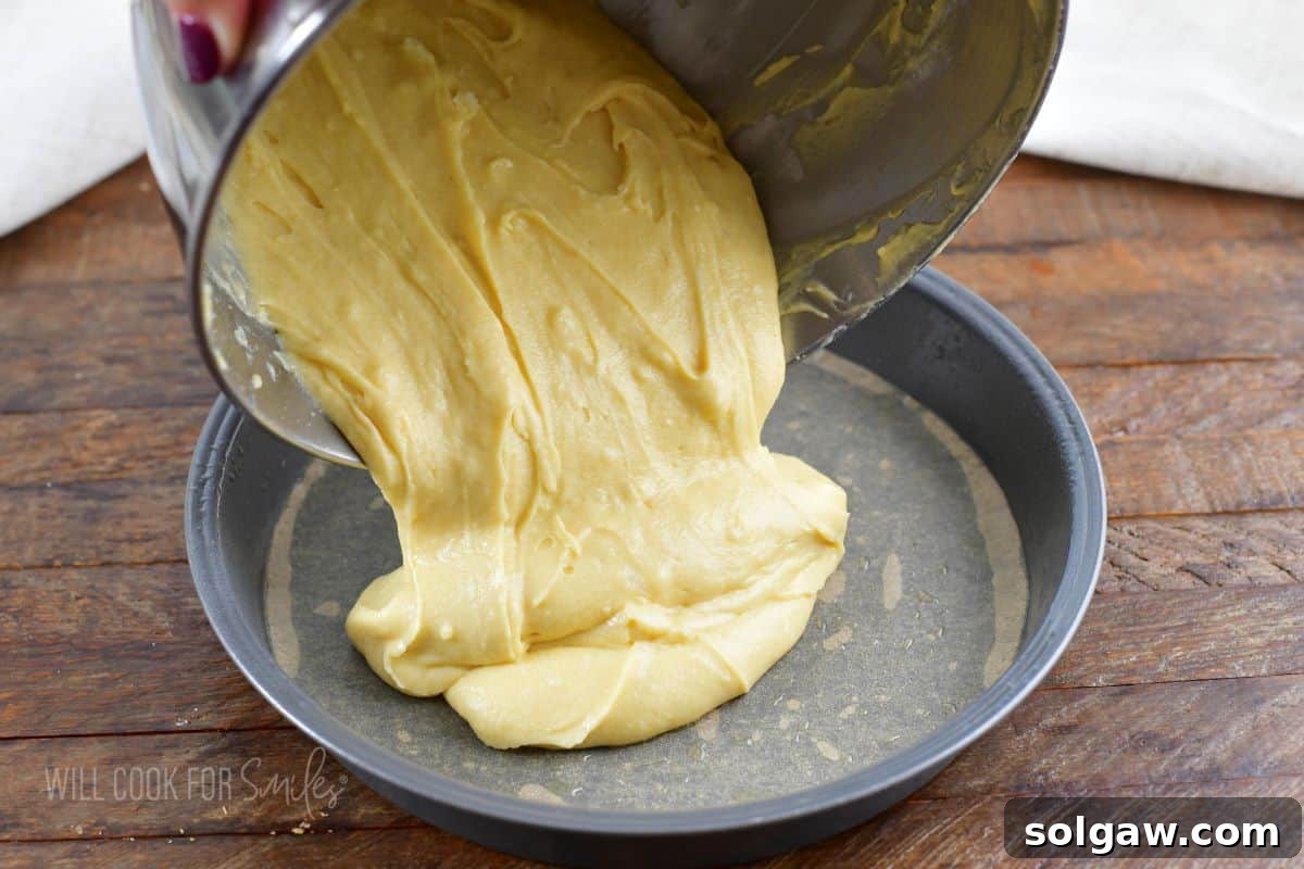 Pouring smooth cake batter into a round cake pan lined with parchment paper, ensuring even distribution.