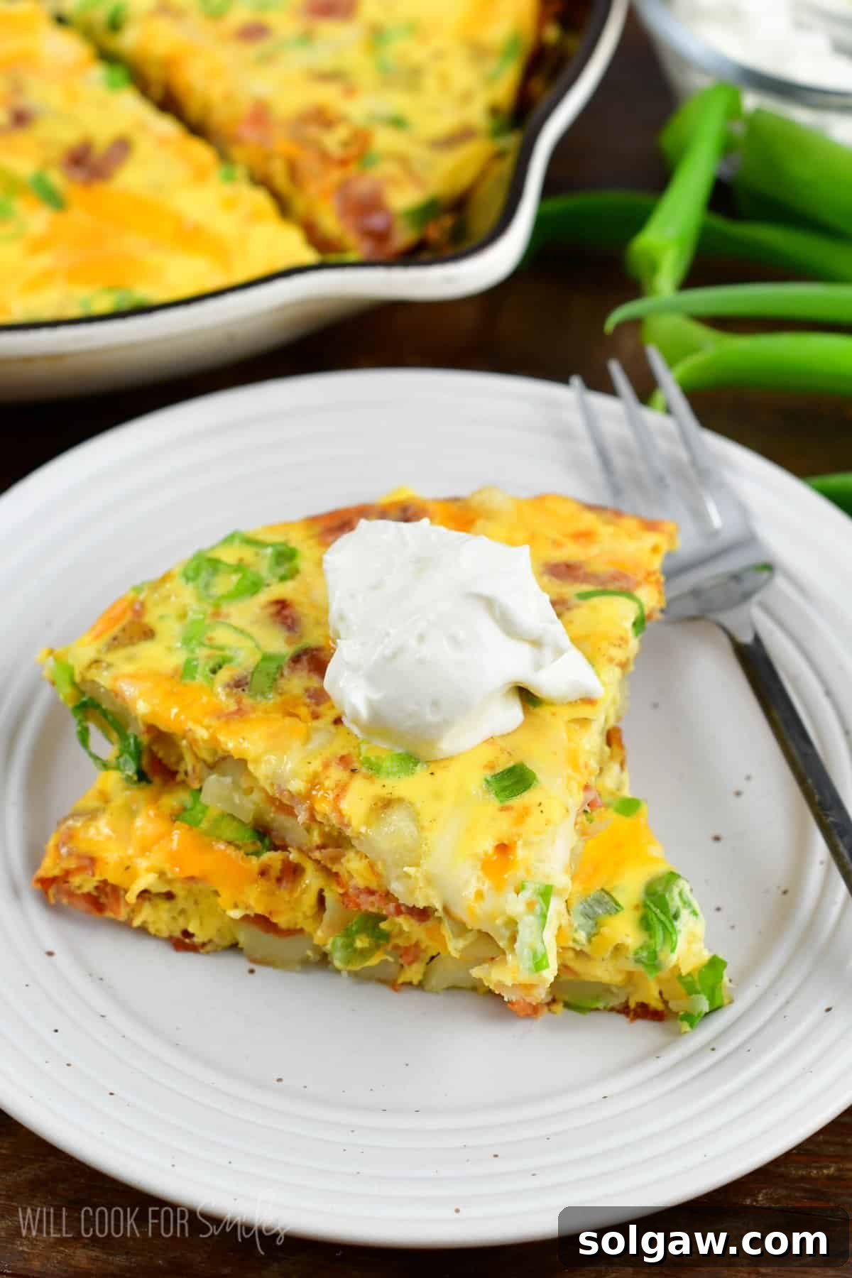 Ultimate Breakfast Potato Skillet 7 Two triangular slices of a loaded breakfast bake, stacked on a white plate with a dollop of sour cream on top, ready to be enjoyed.