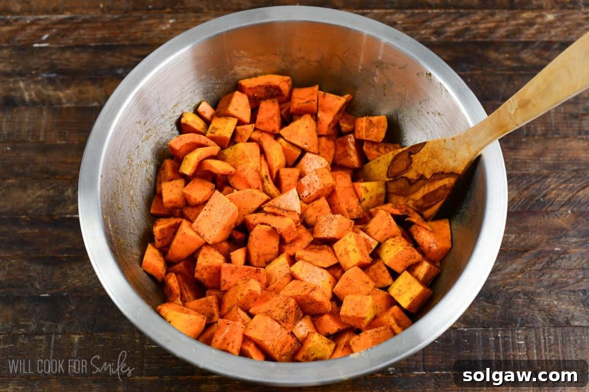 honeynut squash cut up in a metal bowl with spices and a wooden spoon on a wood surface.