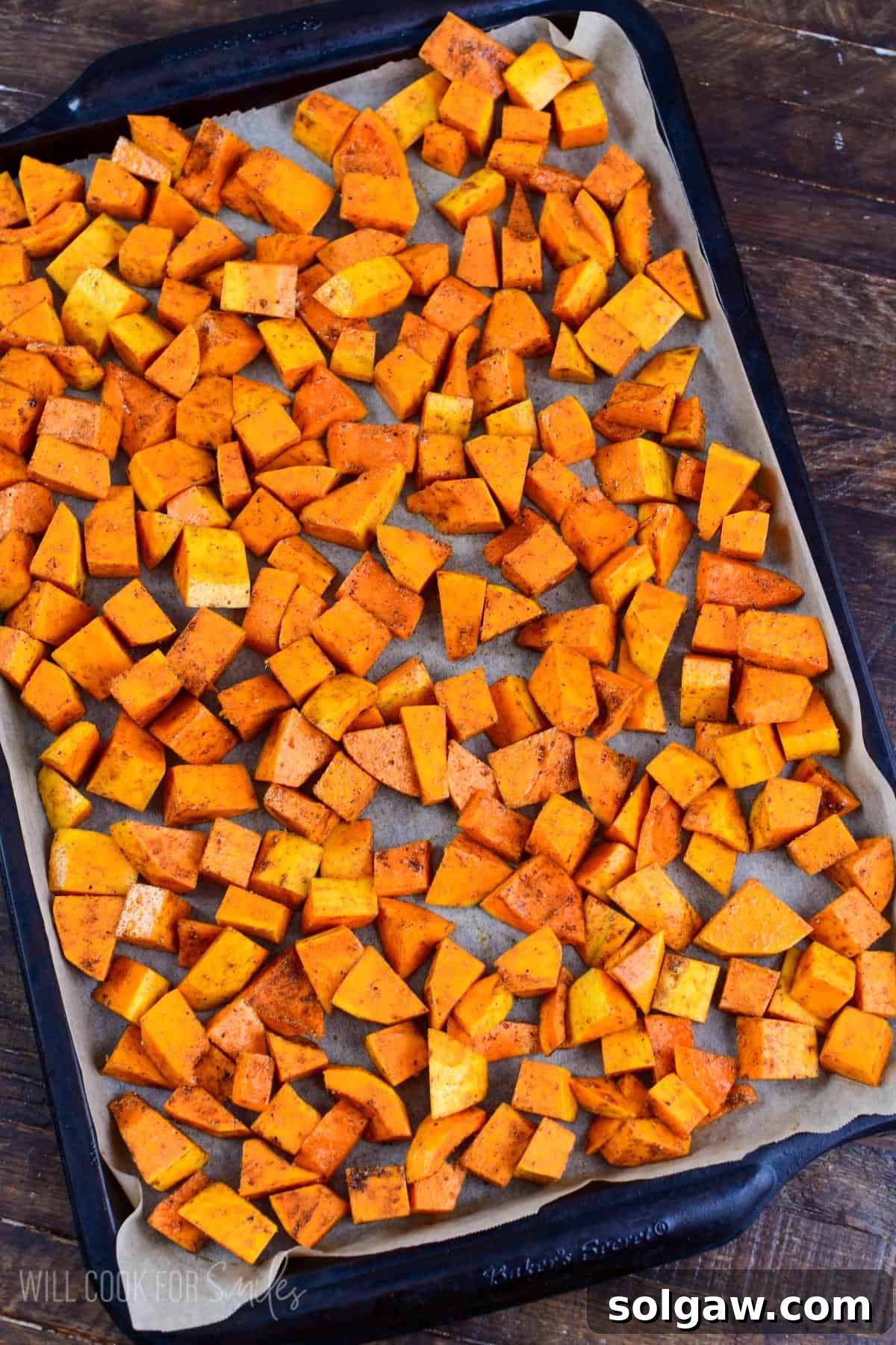 Honeynut squash spread on a parechment paper lined baking sheet on a wood surface.
