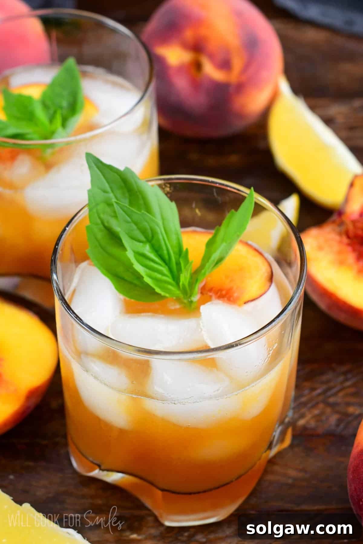 Peach smash bourbon in a glass with ice and peaches and mint on top as garnish.