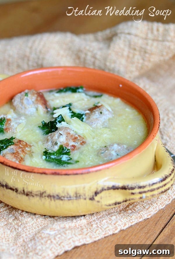A wide shot of Italian Wedding Soup with turkey meatballs, kale, and orzo, presented in a rustic bowl on a wooden surface.