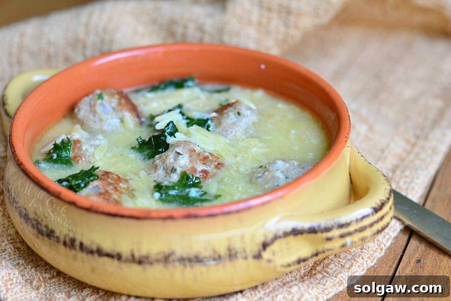 Close-up view of Orange and tan clay crock with Italian Wedding Soup with turkey meatballs and Orzo sitting on a tan table cloth on a wood table