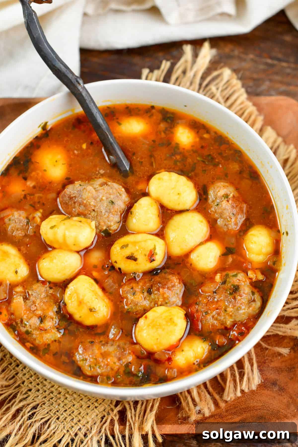 Italian meatballs and gnocchi soup in a bowl with a spoon on wooden plate.
