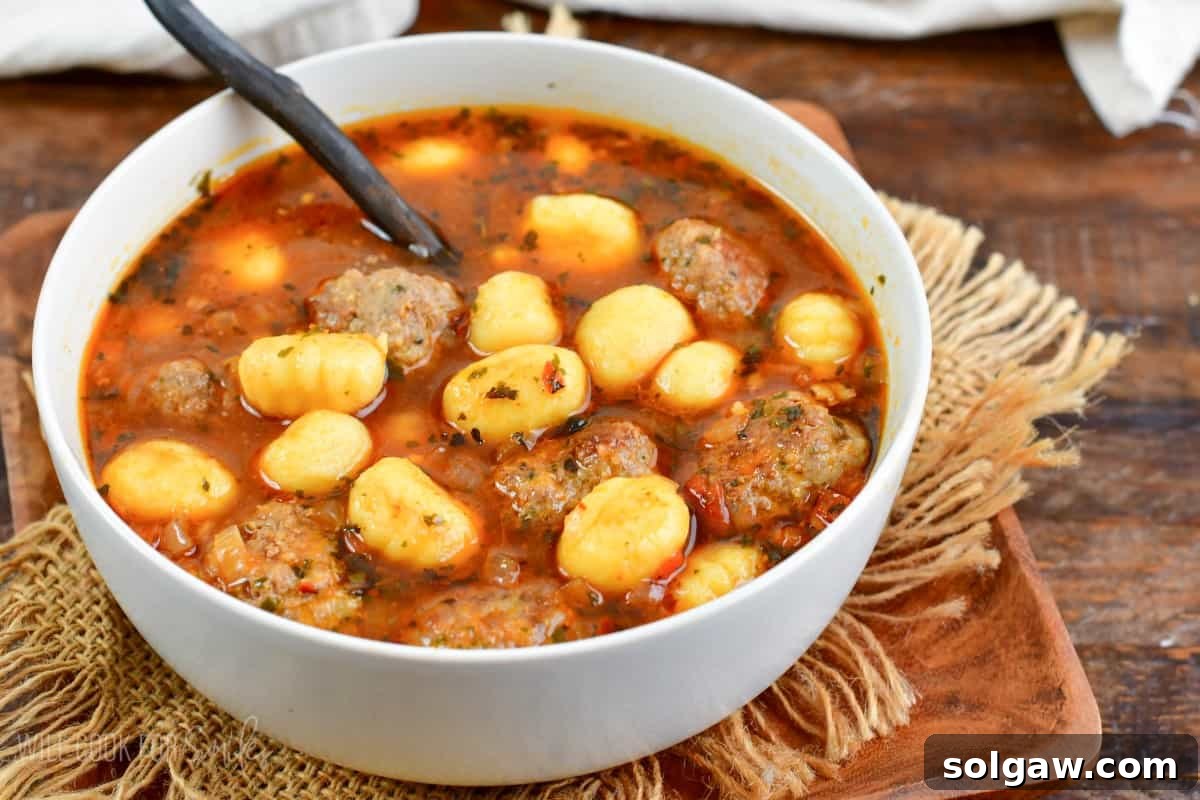 meatballs and gnocchi soup in a bowl on a wooden plate.
