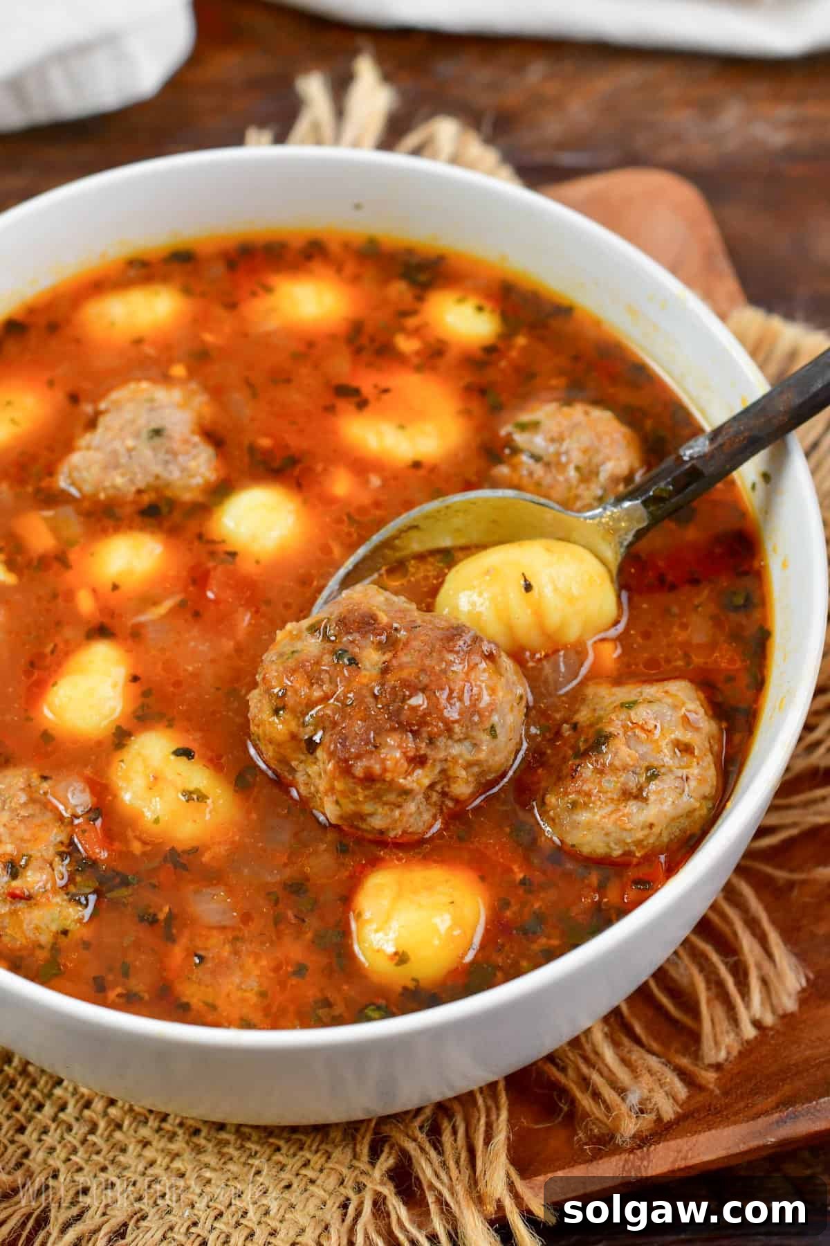 spooning out a meatballs and some gnocchi from the bowl of soup.