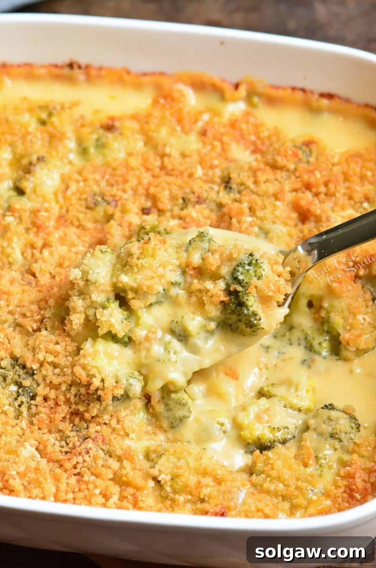 A close-up of a serving of broccoli cheese casserole in a bowl, with a spoon for serving, highlighting its cheesy and crunchy topping.