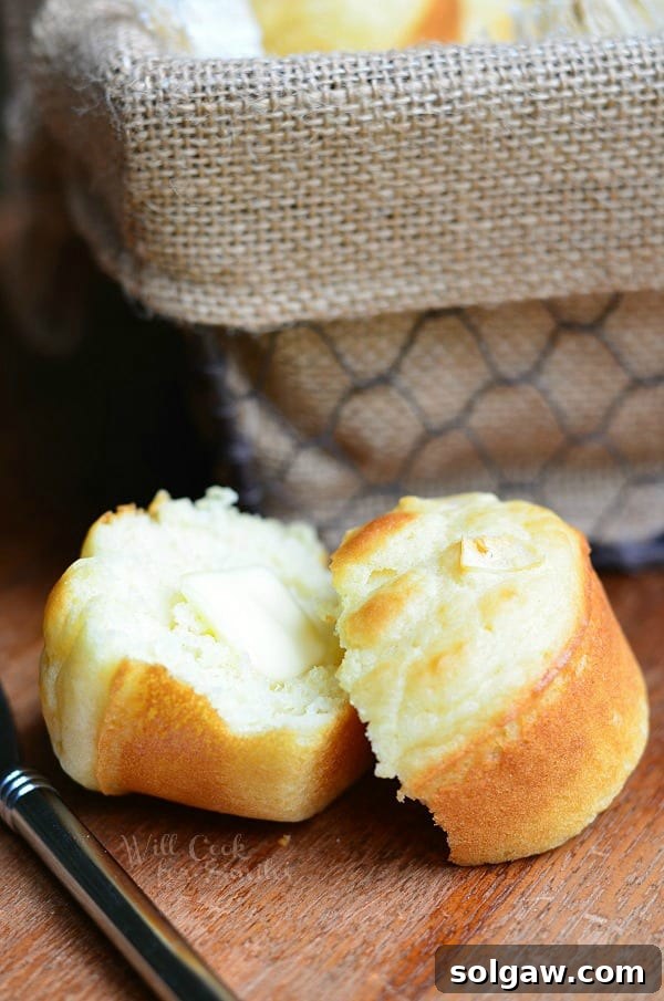 Stacked roasted garlic dinner muffins on a rustic wooden board with herbs.