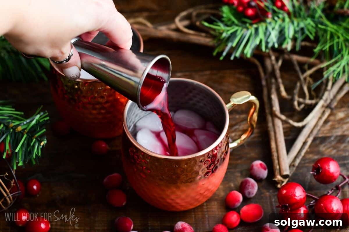 Adding cranberry to a copper mug with the vodka ice on a wood surface with cranberries.