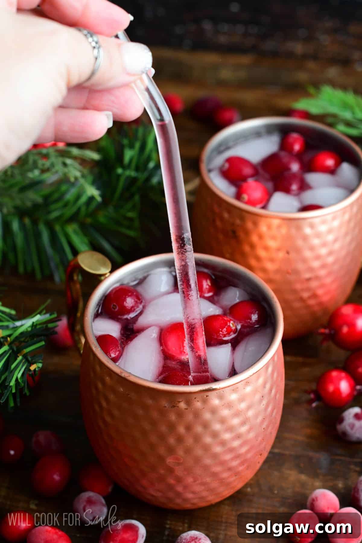 two copper mugs with cranberry Moscow mule in them with a straw with some of the mule in it.