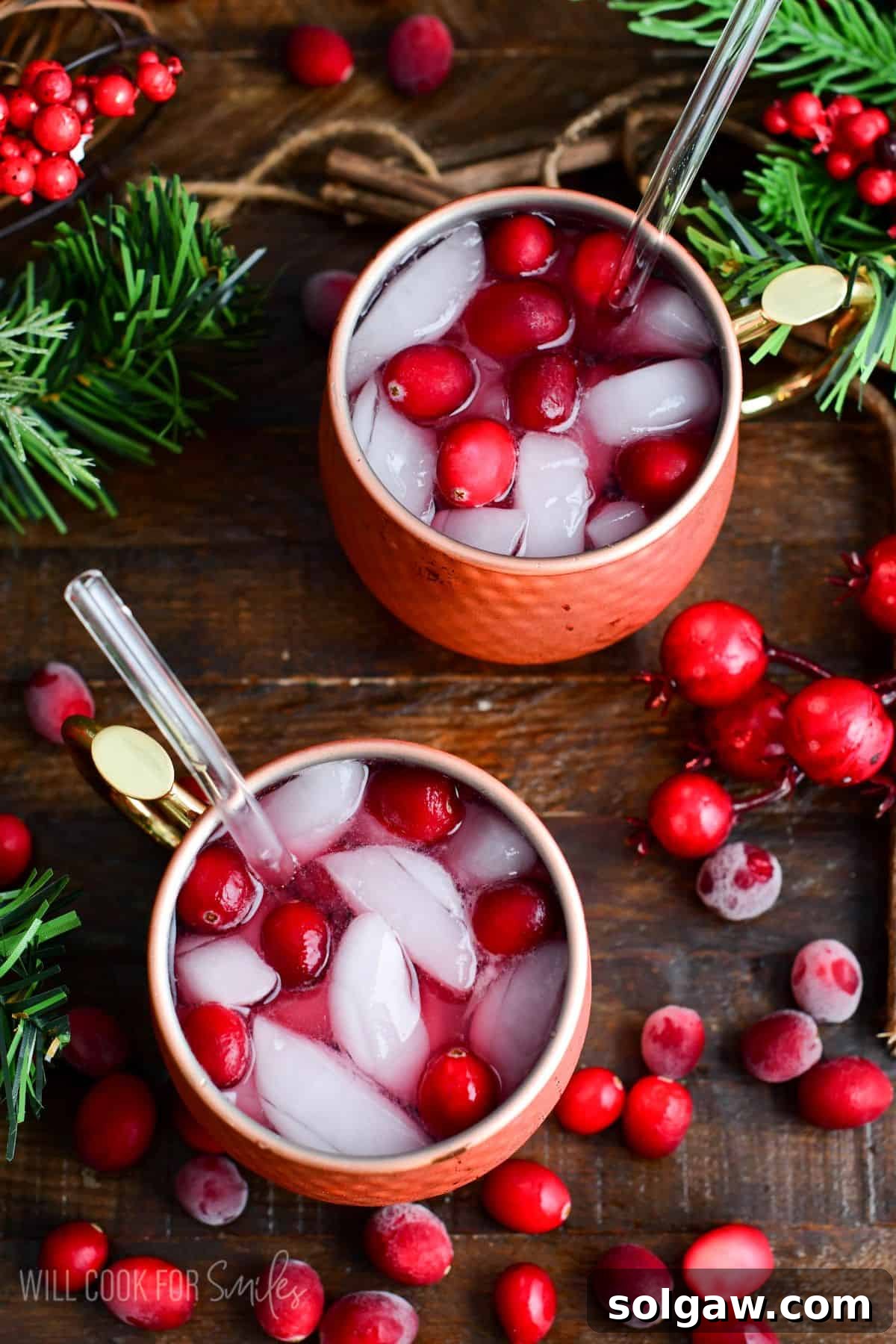 Two copper mugs filled with cranberry Moscow Mules with fresh cranberries and ice and a straw.