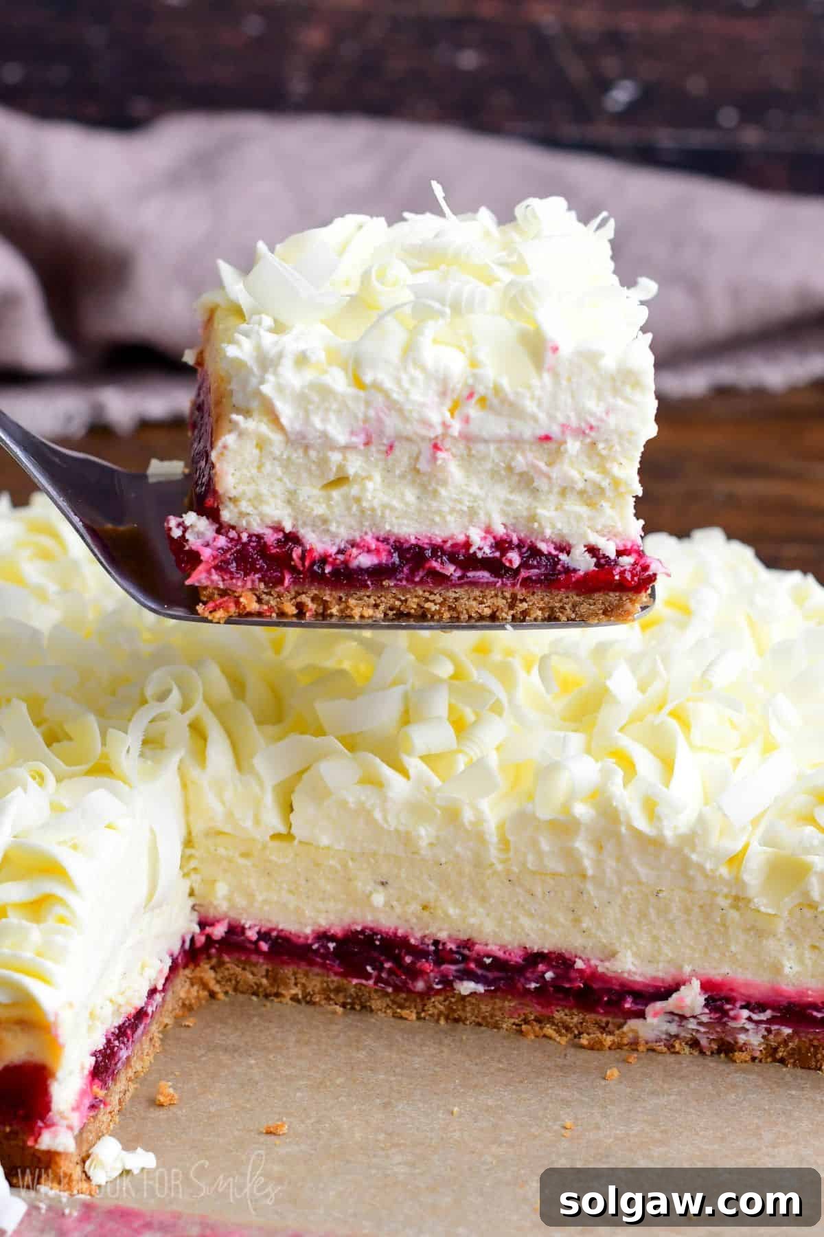 A perfectly cut Christmas Cheesecake bar, delicately lifted on a spatula, with an array of uncut bars waiting invitingly in the background on a festive table setting.