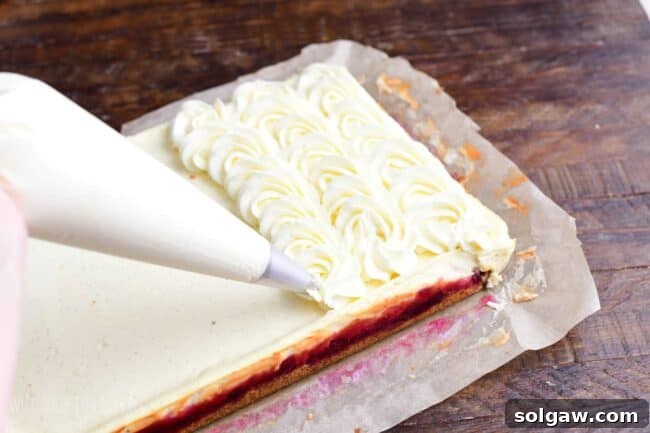 Elegant piping of the fluffy white chocolate mousse frosting onto the chilled Christmas cheesecake bars, creating a beautiful and festive top layer.