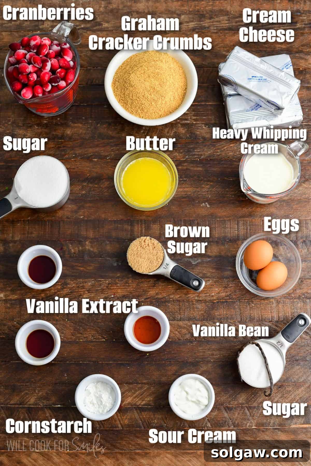 An organized display of fresh cranberries, graham crackers, cream cheese, vanilla bean, and white chocolate melting chips, all key ingredients for the Christmas Cheesecake bars, neatly arranged on a rustic wooden surface.