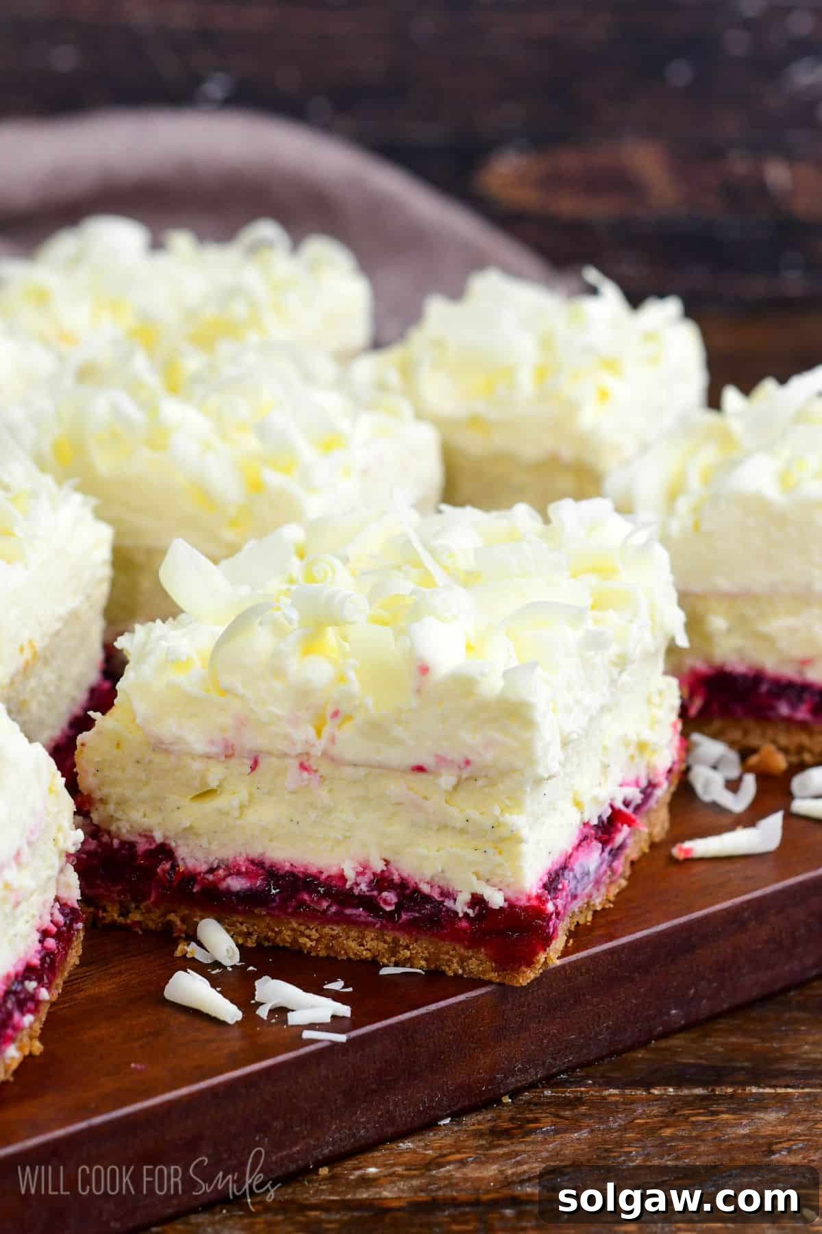 A stunning close-up of beautifully cut Christmas cheesecake bars, adorned with delicate white chocolate shavings, presented on a rustic wooden surface.
