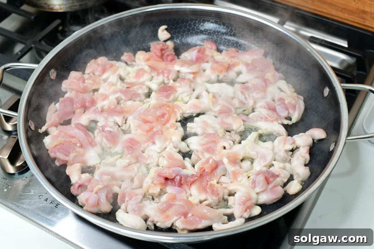 sautéing thinly sliced chicken thigh meat in a large cooking pan.