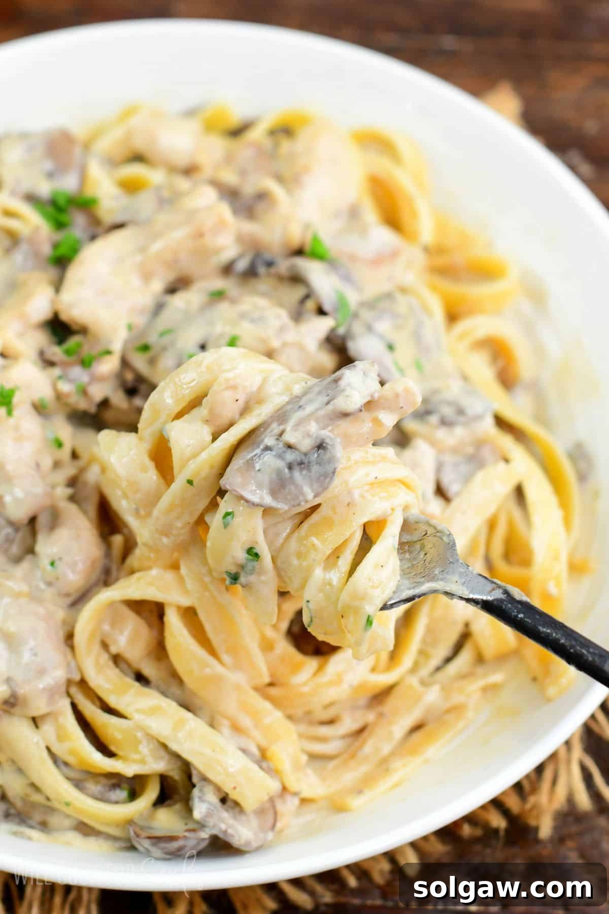 scooping some creamy pasta with chicken and mushrooms with a fork.