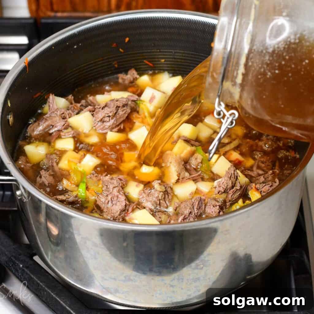 adding clear beef broth to the pot with beef, cabbage, and vegetables. 
