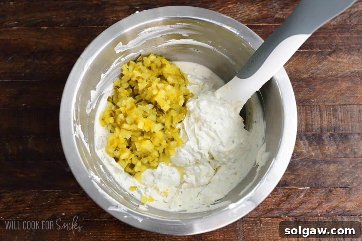Adding diced pickles to a metal bowl on a wood surface,
