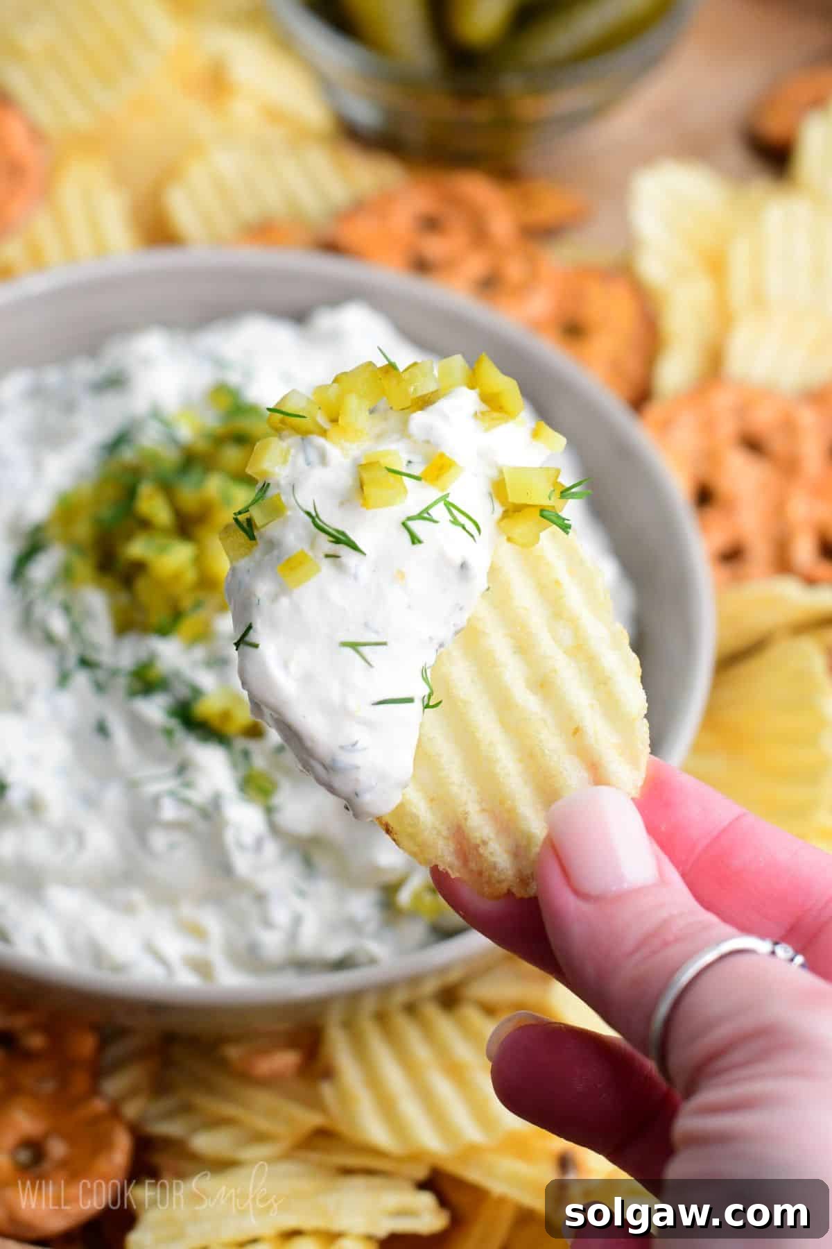 Pickle dip scooped with a chip and the bowl of dip in the background.