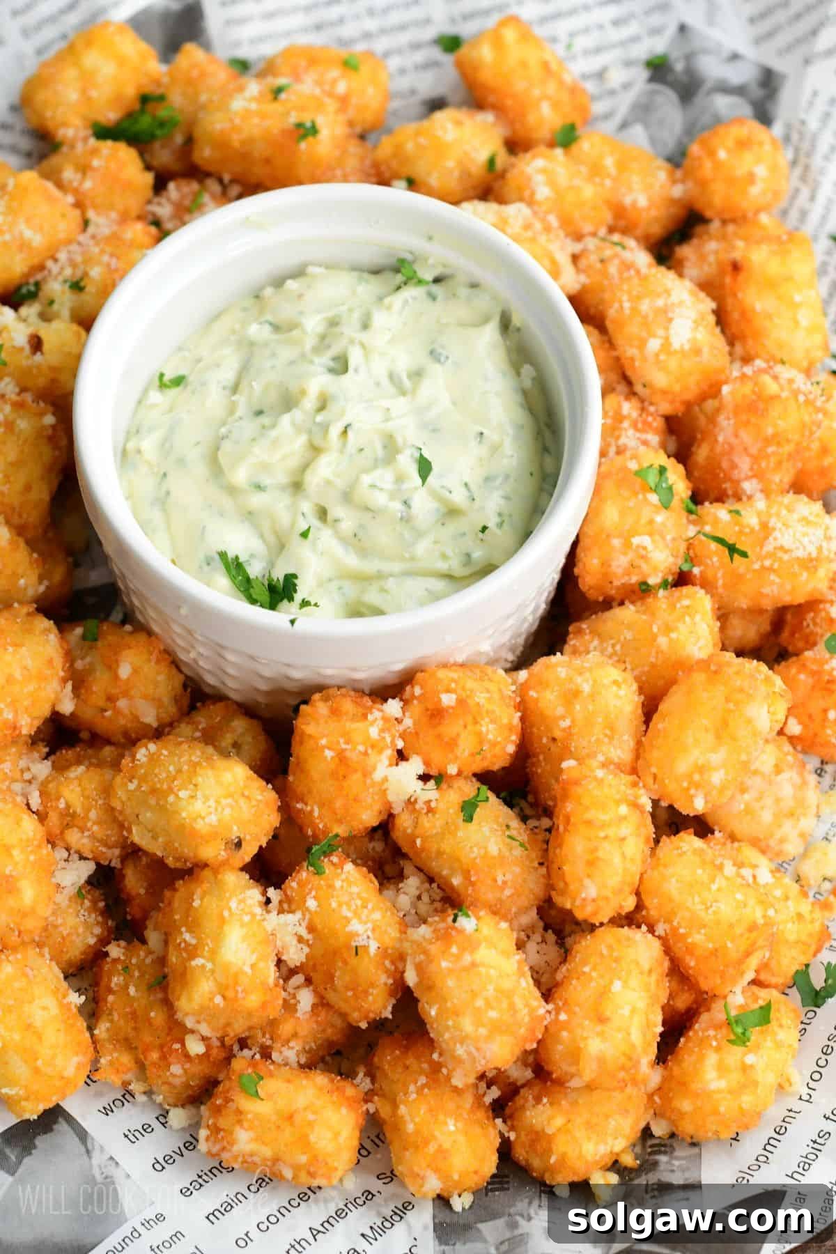 Truffle tater tots on a lined tray with a garlic herb aioli in a bowl in the middle.