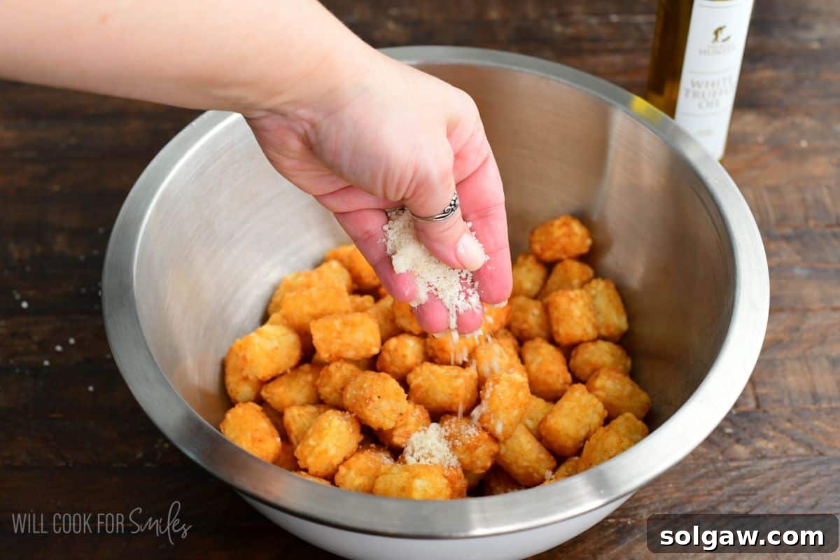 Adding parmesan cheese to a metal bowl of cooked tater tots.