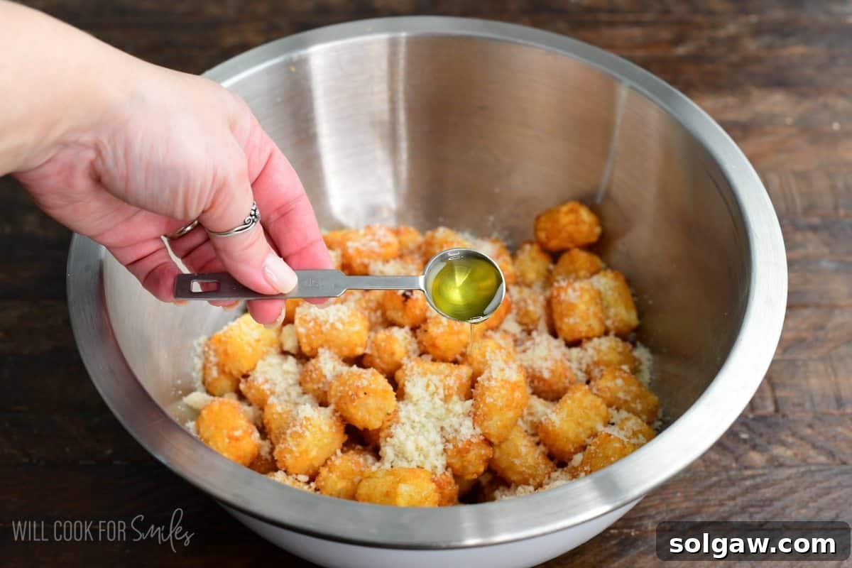 Adding the truffle oil to the bowl of cooked tater tots and parmesan cheese.