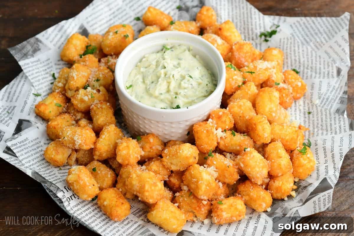 Truffle tater tots on a tray with a garlic herb aioli in a bowl in the middle.
