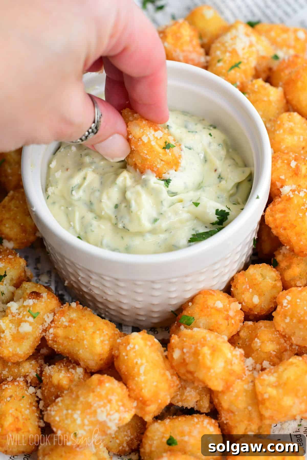 Dipping a truffle tater tot into the bowl of garlic herb aioli on the tray.